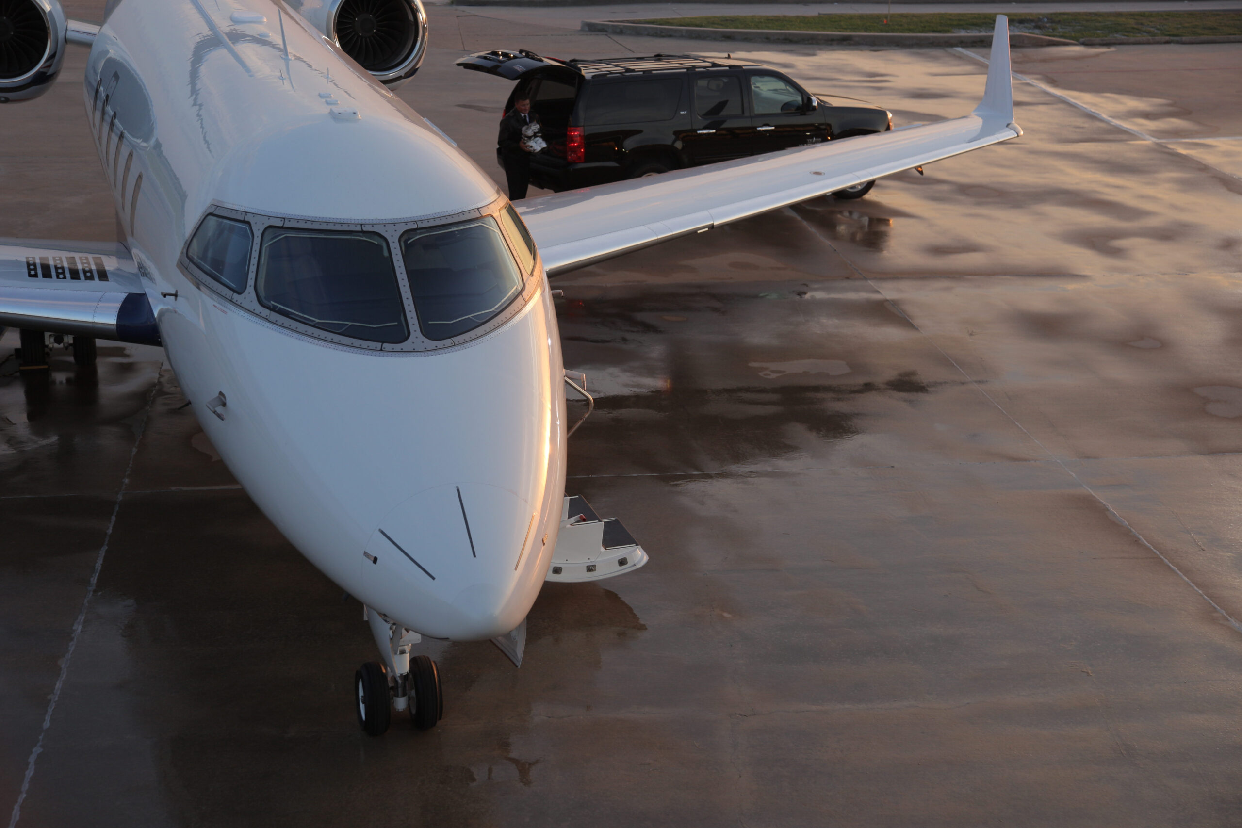 Challenger 300 in twilight with a wet pavement tarmac and SUV unloading items from the back