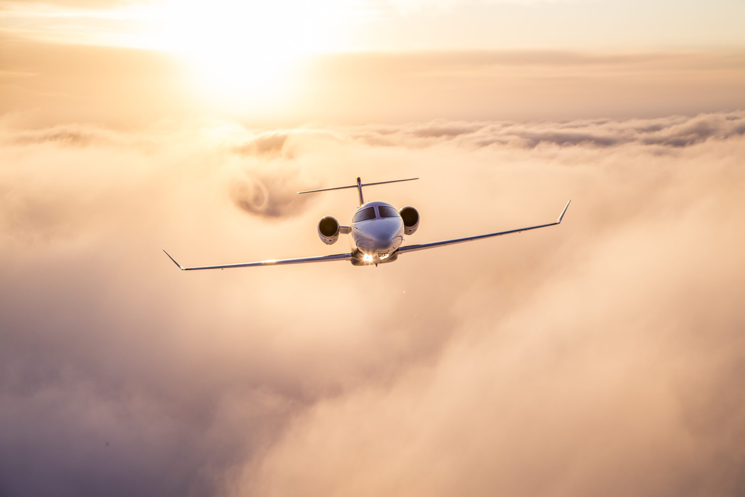 A learjet flies headon through rose colored clouds starting to spiral behind